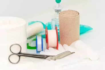 Ein Set aus Wundversorgungsmaterialien, darunter Binden, Scheren und Desinfektionsmittel, liegt auf einem Tisch.