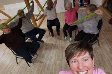 Eine Gruppe Menschen nimmt an einem VHS-Kurs teil und nutzt grüne Fitnessbänder zur Bewegungsgymnastik.