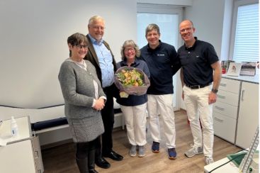 Fünf Personen in einem Behandlungsraum posieren lächelnd mit einem Blumenstrauß. Auf dem Bild zu sehen: Anja Herder-Peyrounette, Dr. Harald Menker, Dorothee Massing,  Dr. Stergios Tsolakidis, Dr. Wilhelm Litz