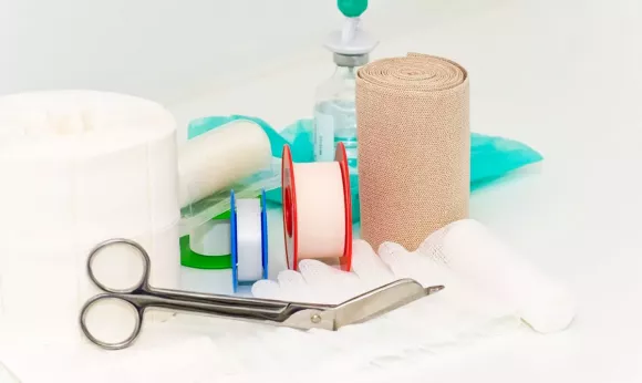 Ein Set aus Wundversorgungsmaterialien, darunter Binden, Scheren und Desinfektionsmittel, liegt auf einem Tisch.