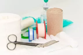 Ein Set aus Wundversorgungsmaterialien, darunter Binden, Scheren und Desinfektionsmittel, liegt auf einem Tisch.