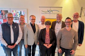 Eine Gruppe von acht Personen steht lächelnd vor einem Banner der Gesundheitsregion Siegerland.