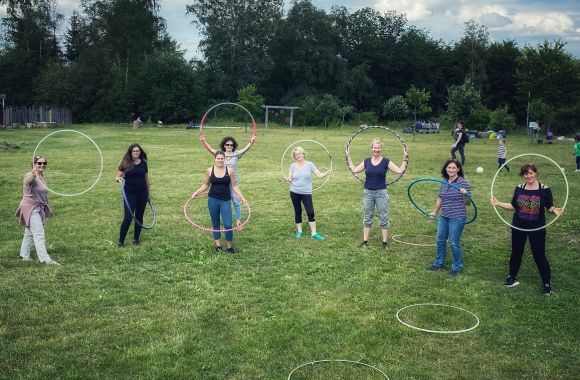 Eine Gruppe von Frauen steht mit Hula-Hoop-Reifen im Freien auf einer grünen Wiese.