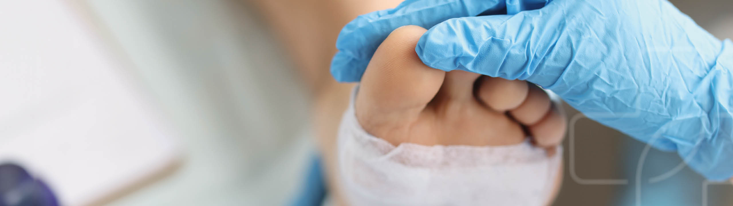 Eine Hand im Handschuh untersucht einen Verband an einem Fuß.