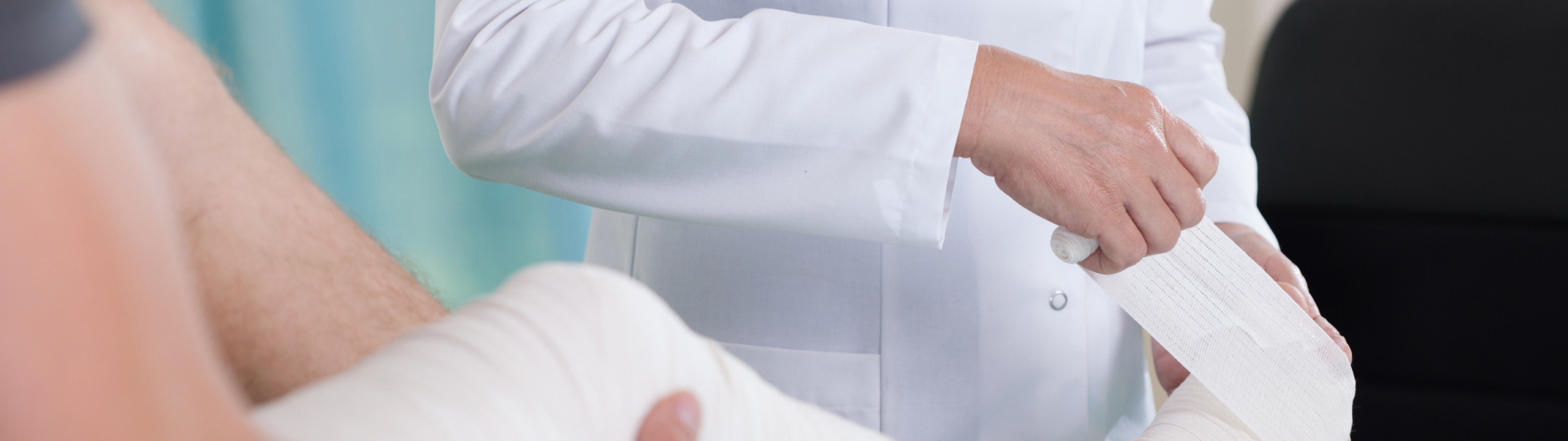 Ein Arzt wickelt einen Verband um das verletzte Bein eines Patienten.