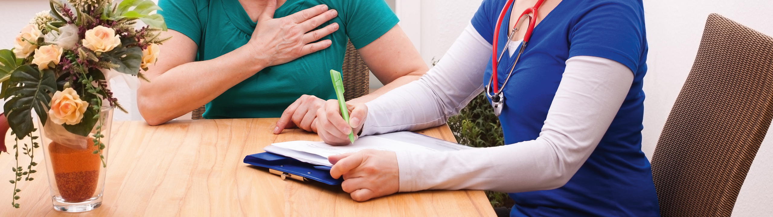 Eine Ärztin schreibt während eines Gesprächs mit einer Patientin an einem Tisch mit Blumen.
