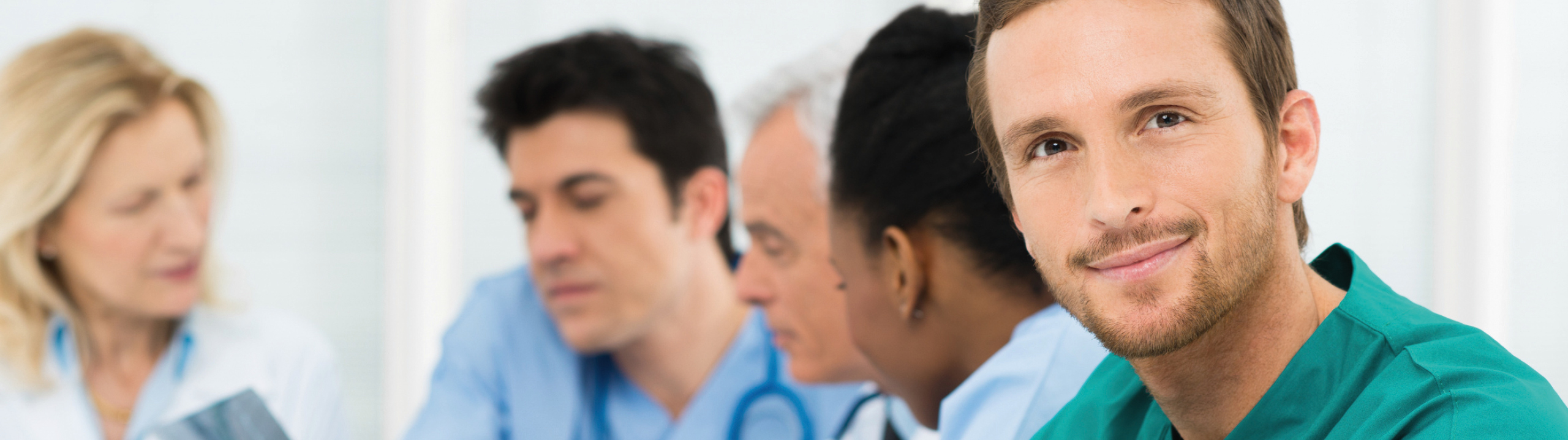 Eine Gruppe von Medizinern diskutiert fokussiert, während ein lächelnder Arzt im Vordergrund die Kamera anschaut.