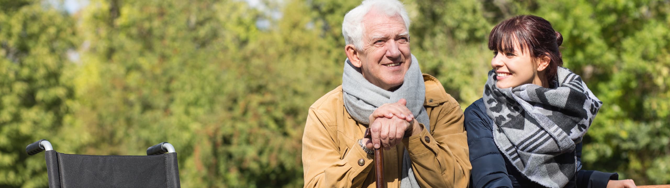 Ein älterer Mann sitzt mit einer lächelnden Frau im Freien, beide tragen Schals.