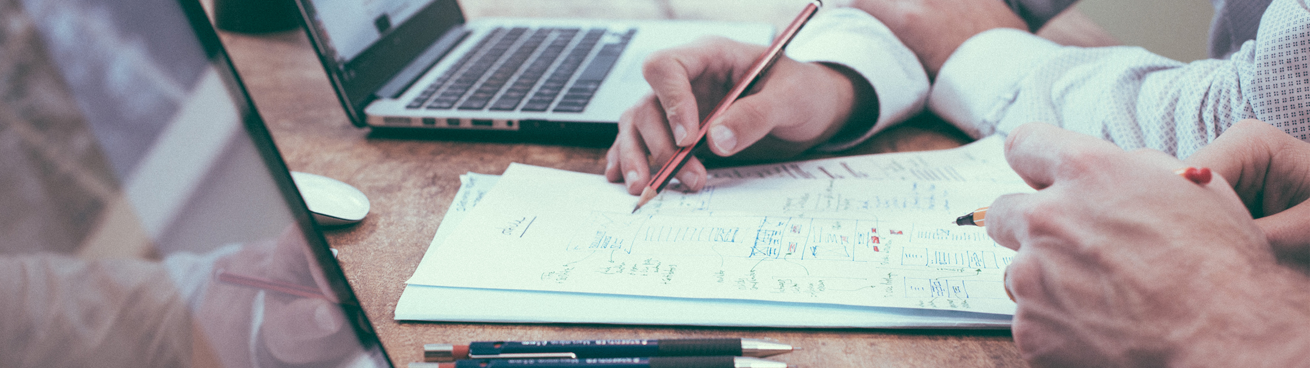 Zwei Personen arbeiten gemeinsam an einem Tisch an Papieren und einem Laptop, während sie Notizen machen.