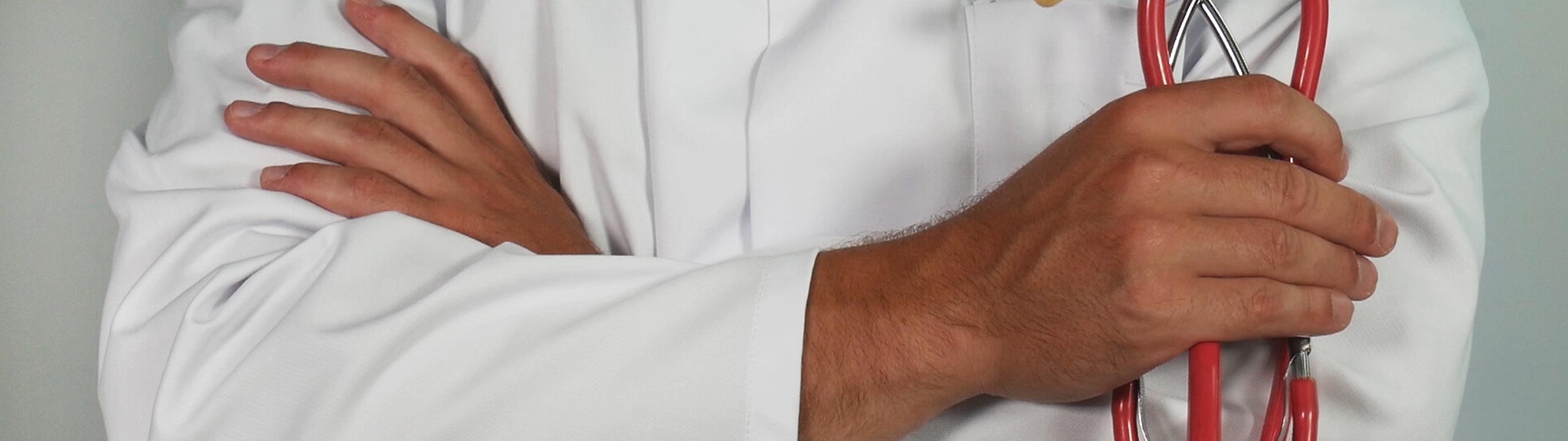 Ein Arzt in weißem Kittel steht mit verschränkten Armen und hält ein Stethoskop.